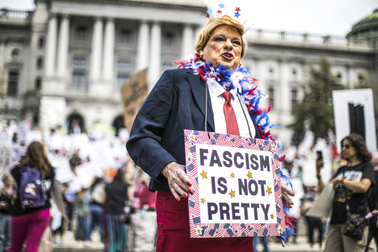 지난 19일(현지시간) 펜실베이니아주 해리스버그에 있는 주 의사당 앞에서 트럼프 복장을 한 시위자가 항의 팻말을 들고 있습니다. AP 연합뉴스